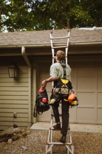 Person on a stable ladder attaching weatherproof lights to a home’s roofline with plastic clips.