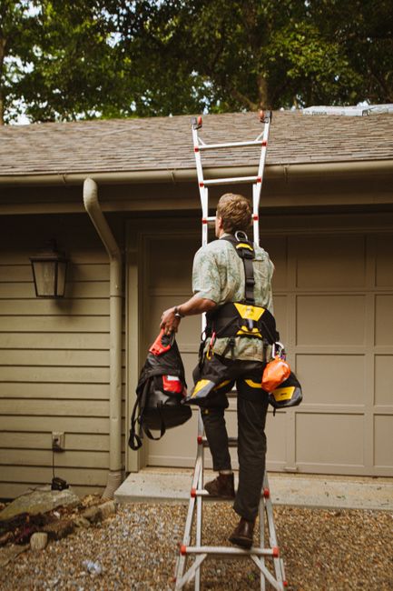 Person on a stable ladder attaching weatherproof lights to a home’s roofline with plastic clips.